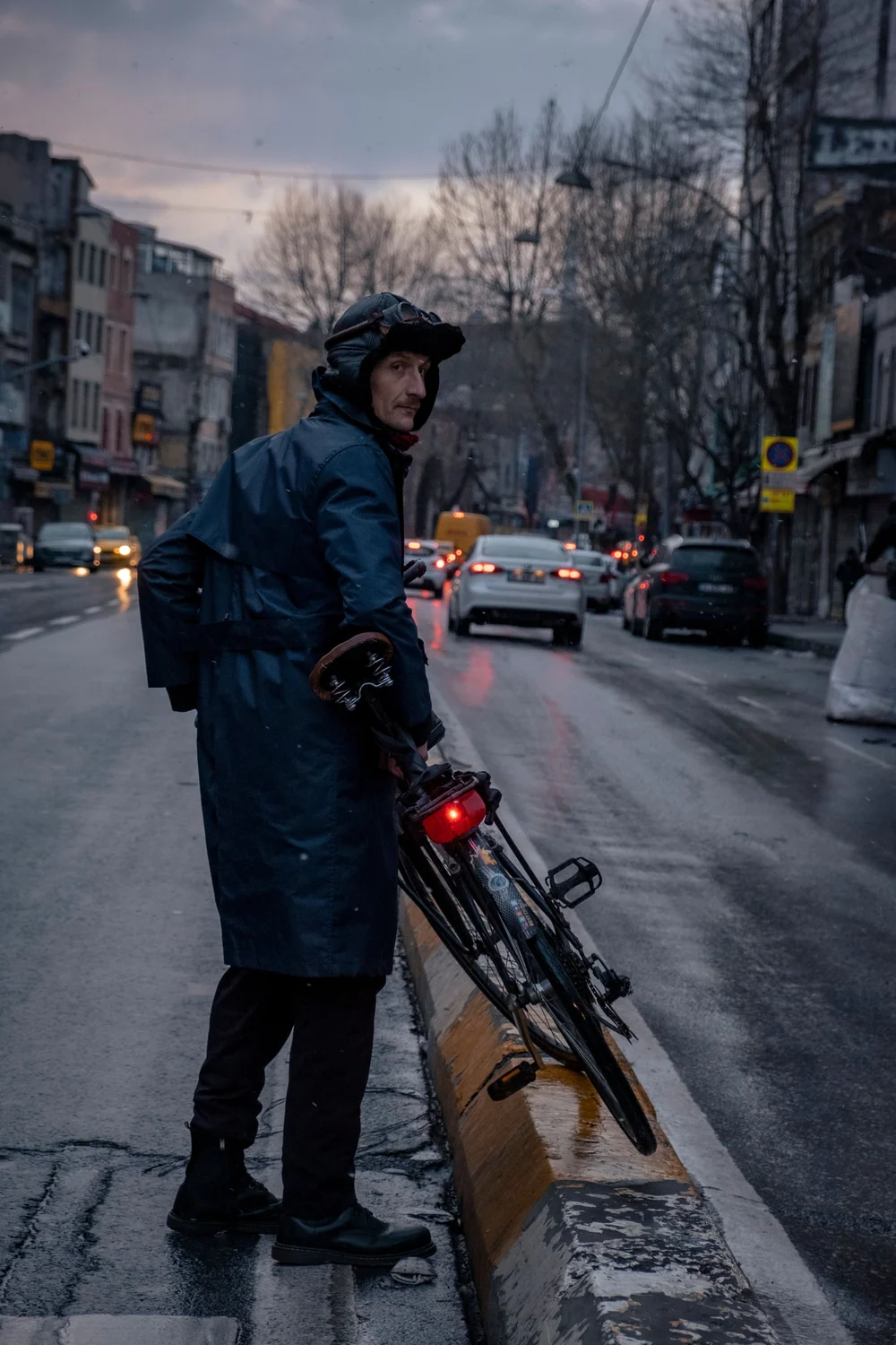 Radfahrer mit Helm und beleuchtetem Fahrrad in einer regennassen Stadt bei Dämmerung